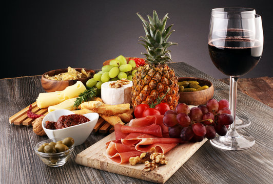 Italian antipasti wine snacks set. Cheese variety, Mediterranean olives, pickles, Prosciutto di Parma with grapes, wine in glasses over black grunge background