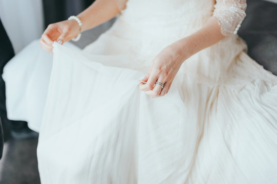 Closeup toned photo of beautiful bride tying up her wedding dress