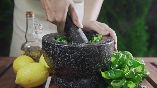 Housewife grinds the basil for pesto sauce outside, cooking food, spicy food, vegetarian meal