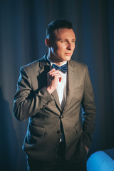 Stylish bridegroom in gray suit and butterfly posing in hotel