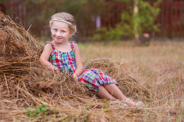 Naklejka na ściany i meble happy child girl in country style in hat relaxing on summer field with hay stacks