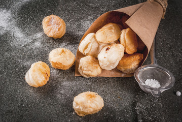 Homemade baking, puff pastries. Trendy food. Cronuts popcorn, puff donuts holes, in paper bag, with powdered sugar. On a dark stone table. Copy space