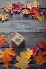 Obraz premium cardboard box tied with string on a bow on a wooden background in autumn leaves, holiday gift on Thanksgiving Hellouin. view from the top. copy space
