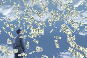 Business man looking at money rain against sky with clouds
