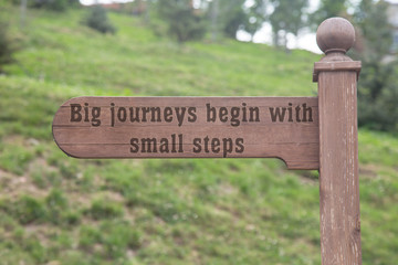 Big journeys begin with small steps text wooden sign with a forest background. wooden direction sign 