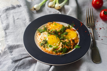 Fried eggs on the plate with cherry tomatoes,  spices and green onions in rustic style. Healthy breakfast, selective focus