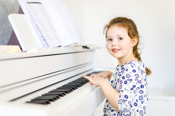 Beautiful little kid girl playing piano in living room or music school