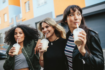 Three young females having ice coffee on city street