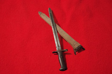 WWI bayonet and scabbard, unsheathed, on red background