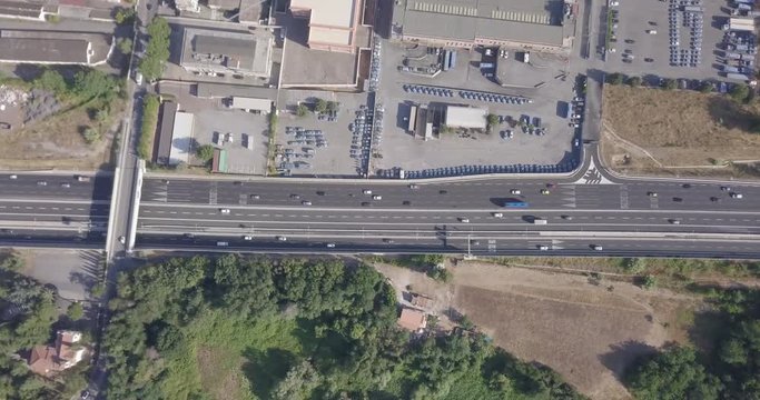 Vista aerea ortogonale del passaggio di automobili e camion lungo un autostrada italiana che collega due grandi citt&agrave;. Ai lati dell'autostrada sono presenti un parcheggio e un campo in parte coltivato