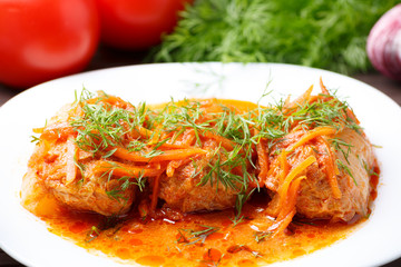 Cabbage rolls in tomato gravy with carrots and fresh dill on a white plate. Сlose-up.