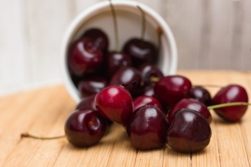 Spilled bowl of ripe very dark red and black cherries on wooden table