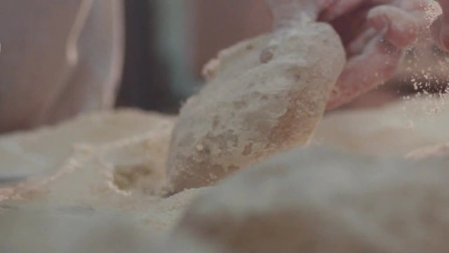 Extreme close up view of baker&rsquo;s hands one by one kneading the pieces of dough in the flour on the table. Beautiful process, daily routine. Baking manufacture, traditions. Bread-making industry.