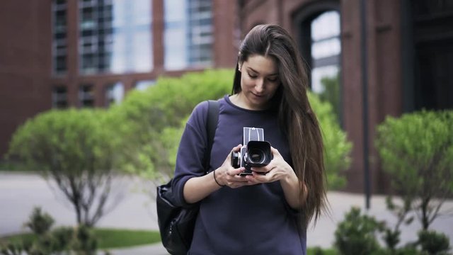 Portrait of a young beautiful woman holding an old fashioned camera and walking in the street looking for an inspiration