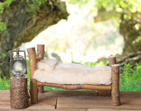 A newborn bed studio photography prop with a railroad lantern and a wooded forest background.  The bed is handmade from a Coral Bark Japanese Maple tree.