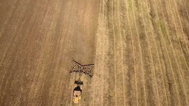 Marvelous aerial shot of a big tractor drawing a spike and a disc harrows to remove wheat straw and to do a  tillage in Eastern Europe in a sunny day in summer. The landscape looks gorgeous