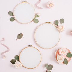 Fototapeta na wymiar Embroidery frames with beige rose flower buds and eucalyptus on pale pastel pink background. Flat lay, top view decorated concept.