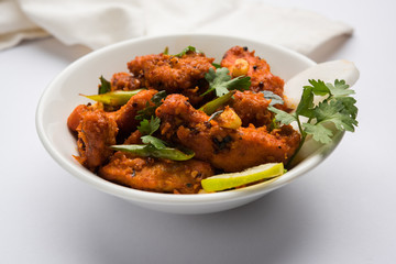 Chicken 65 - spicy deep fried Bar appetizer or quick snack from India in a bowl or plate over white...