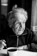 Black-and-white portrait of an elderly woman drinking tea at home.