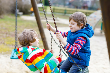 Two little kid boys having fun with chain swing on outdoor playground