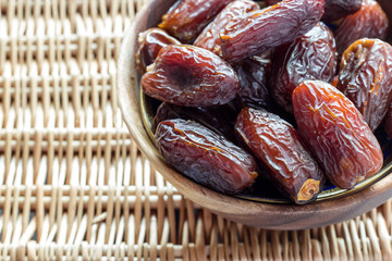 Fresh dates in Madjul in a wooden bowl in the upper right corner, on a woven background. Selective...
