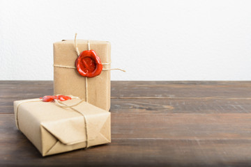 Two gifts wrapped in craft paper with rope and red sealing wax over brown wooden table