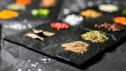 Large selection of different colorful contrast spices and seeds on slate against black background