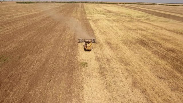 Wonderful aerial shot of a big tractor drawing a spike and a disc harrows to remove wheat straw and to do a  tillage in Eastern Europe in a sunny day in summer. The landscape looks great