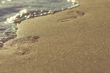 Barefoot footprints on the beach with a wave coming in. Summer vacation.