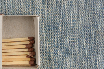 Close-up of a match with a brown head in a box lying on a light denim