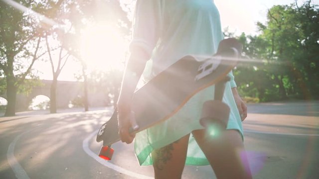 Close up shot of young stylish hipster girl with green hair walking with long board during sunrise, slow motion, gimbal shot