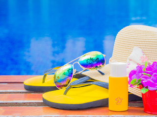 Sunglasses with summer hat, flip flops, sunscreen lotion  and flowers by the swimming pool....