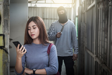 Beautiful young woman holding smartphone and being stalked by man criminal with the knife