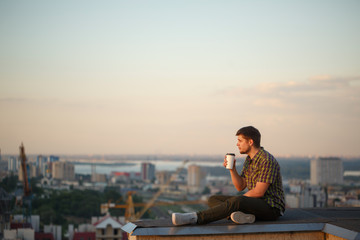 Fototapeta na wymiar Man is drinking coffee on roof in morning