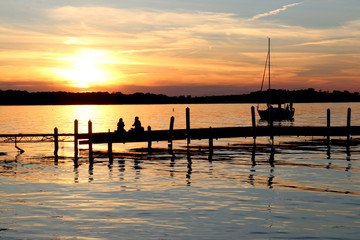 Summer sunset over the lake. Landscape with golden sunset and silhouettes of people enjoying the beautiful evening on a lake Mendota pier in the city of Madison, Wisconsin, USA.