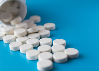 Many pills poured out of the vial on blue background.