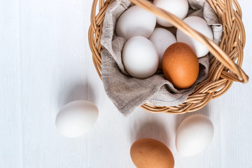 Basket with white and brown natural eggs on white wooden background