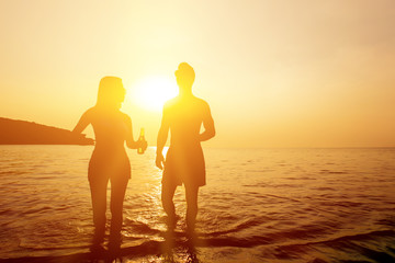 Silhouette of couple walking in seawater at the beach in twilight sunset