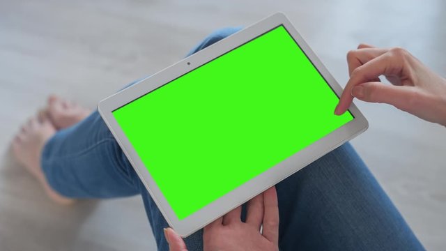 Young Woman in blue jeans sitting on the floor uses Tablet PC with pre-keyed green screen. Few types of gestures - scrolling up and down, tapping, zoom in and out. Perfect for screen compositing