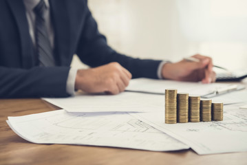 Businessman reviewing document with money and blueprints on the table - real estate and properties investment concepts
