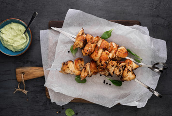 Barbecued chicken breast skewers with avocado sauce on dark background