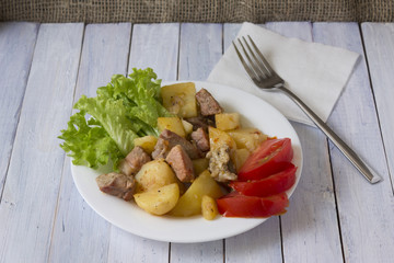 Potatoes with meat and vegetables on a white plate. Tasty and hearty dish.