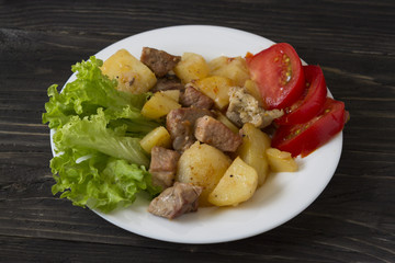 Potatoes with meat and vegetables on a white plate. Tasty and hearty dish.