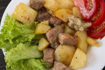 Potatoes with meat and vegetables on a white plate. Tasty and hearty dish.