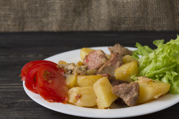 Potatoes with meat and vegetables on a white plate. Tasty and hearty dish.