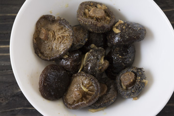 Marinated mushrooms in a white bowl on a wooden table