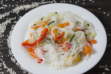 Rice noodles Funchoza with vegetables in a white plate. Traditional Korean cuisine.