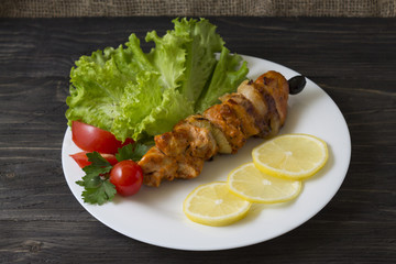 Chicken skewers with vegetables on a white plate. Still life in rustic style. Dish on a wooden table.