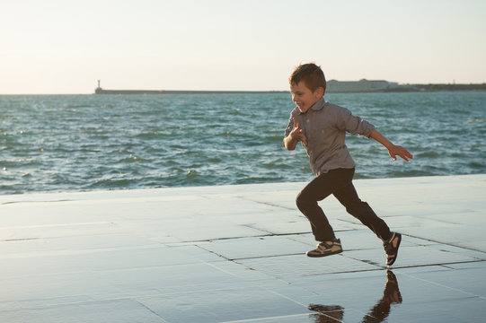 happy little kid running along the sea coast in the city