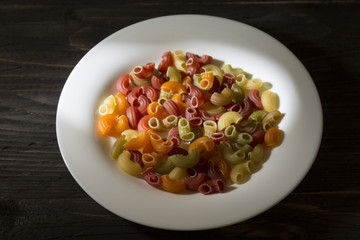 Raw colored pasta in a white plate on a wooden table